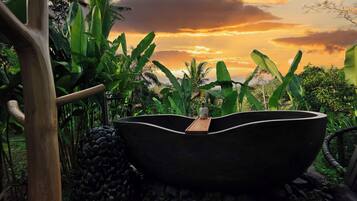Una bañera negra grande rodeada de exuberante vegetación y una estructura de madera.