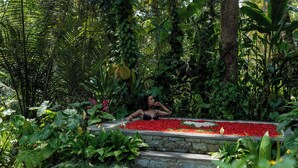 A person relaxing on stone steps surrounded by lush greenery and a flower bed.