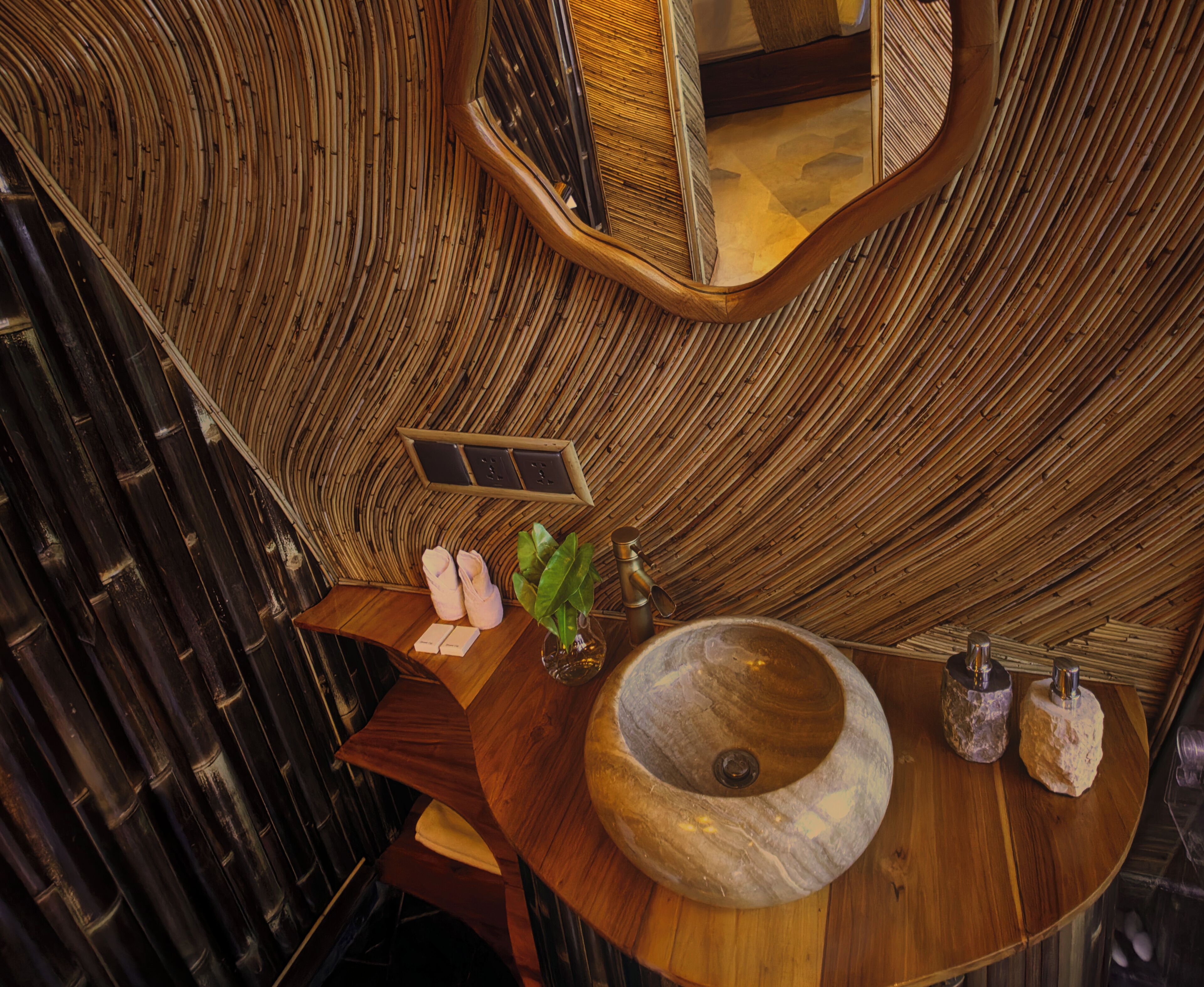 Ein Badezimmer mit einem gebogenen Holz-Waschtisch, einem großen Steinbecken und einem Spiegel darüber.