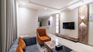 A modern living room with a sofa, armchair, coffee table, and TV. - Taleen Serviced Apartments AlQuds (Riyadh)