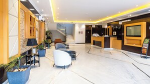 A modern lobby with seating, a reception desk, a staircase, and a TV screen. - Taleen Serviced Apartments AlQuds (Riyadh)