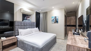 A modern hotel room with a large bed, a desk, a flat-screen TV, and a bathroom with a shower and toilet. - Taleen Serviced Apartments AlQuds (Riyadh)
