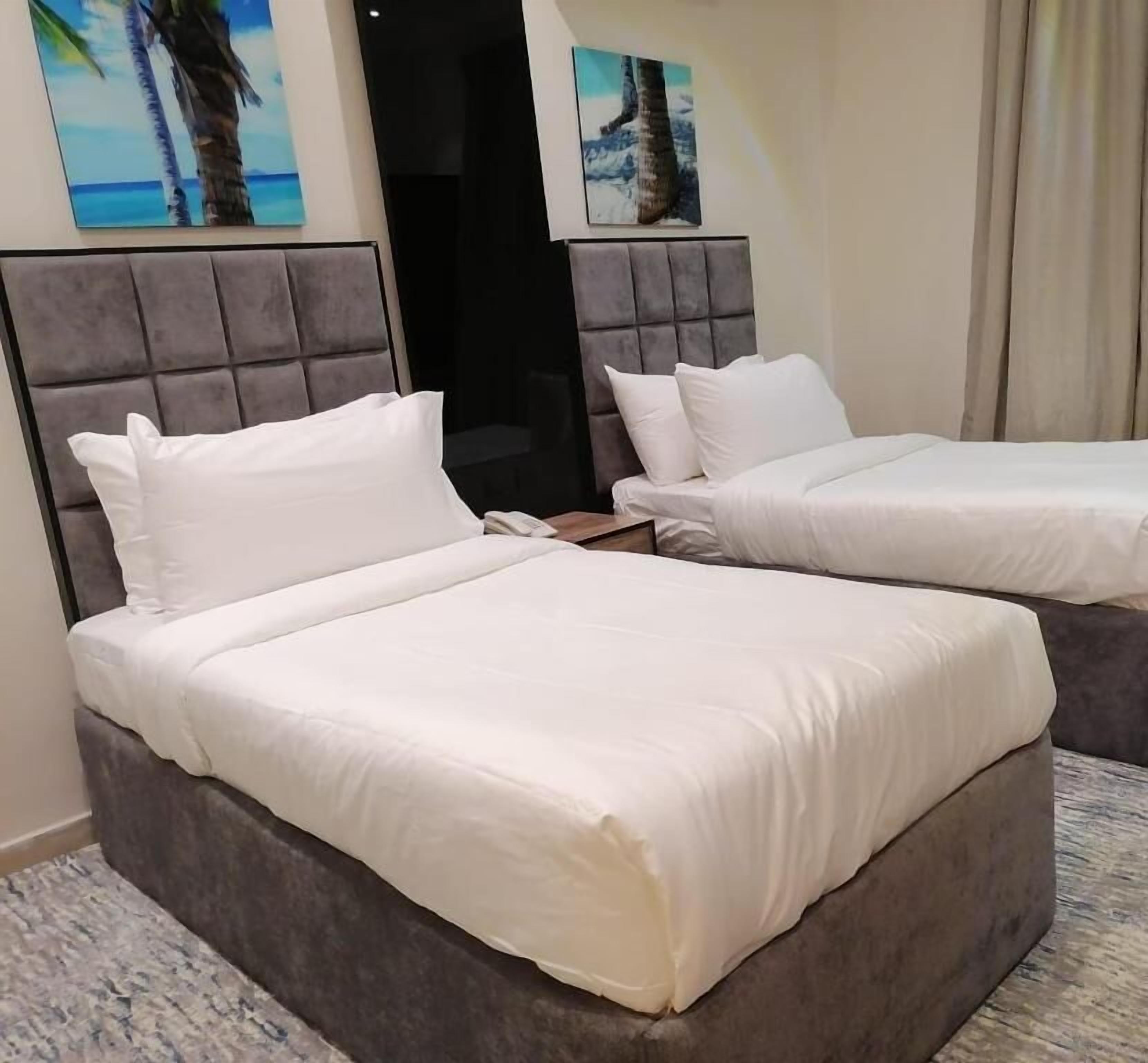 Two beds with grey headboards, white bedding, and a small bedside table.
