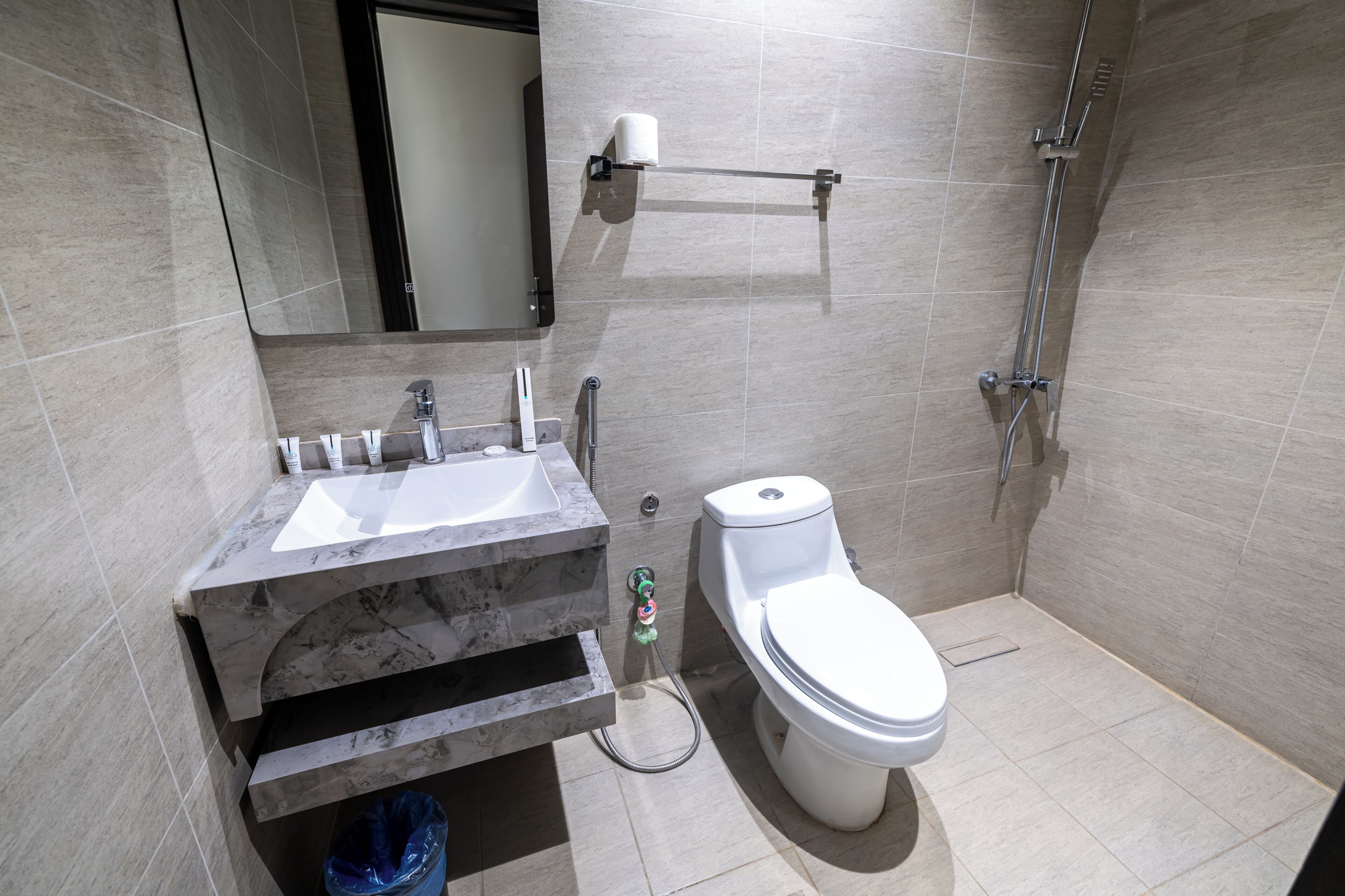 Une salle de bain moderne avec un lavabo en marbre, des toilettes, une douche et un porte-serviettes.