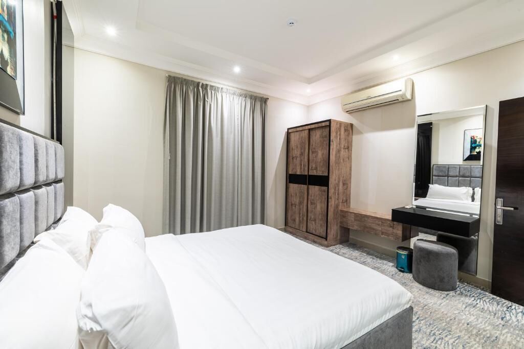 A hotel room with a bed, a wardrobe, a mirror, and a small stool.