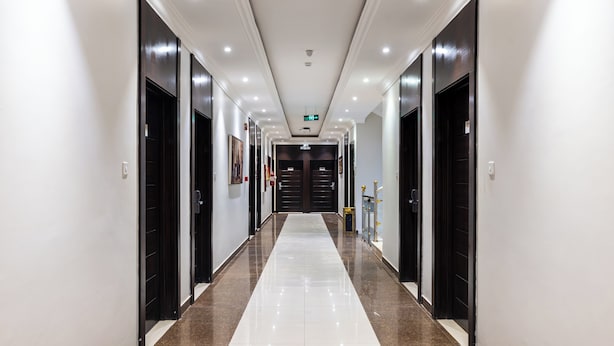 A long, narrow hallway with a polished floor, dark doors on both sides, and recessed lighting on the ceiling. - Taleen Serviced Apartments AlQuds (Riyadh)