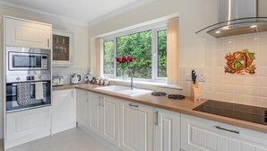 Une cuisine moderne avec des meubles blancs, un four encastré, un micro-ondes, une grande fenêtre donnant sur un espace verdoyant et un crédence décorative.