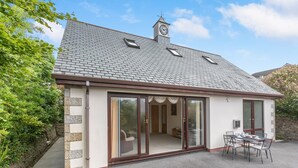 Un bâtiment doté d’un toit en tuiles, d’un clocher et d’un patio aménagé avec une table et des chaises.