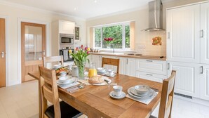 Une cuisine moderne avec des meubles blancs, une table à manger dressée pour le petit-déjeuner et une fenêtre donnant sur un paysage verdoyant.
