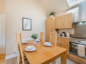 A dining area with a wooden table set for four, a kitchen with modern appliances, and a framed map on the wall. - 2 Bed in Blakeney (oc-54766) (Awre)