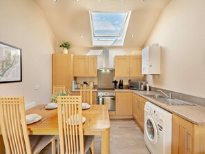 A compact kitchen with wooden cabinets, a dining table with chairs, a built-in washing machine, and a skylight. - 2 Bed in Blakeney (oc-54766) (Awre)