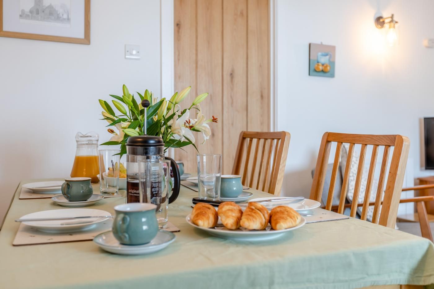A breakfast table set with plates, cups, a coffee maker, and pastries.