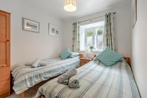 Ein Schlafzimmer mit zwei Einzelbetten, einem Holzschrank, einem Fenster mit Vorhängen und einem kleinen Tisch mit Lampe.