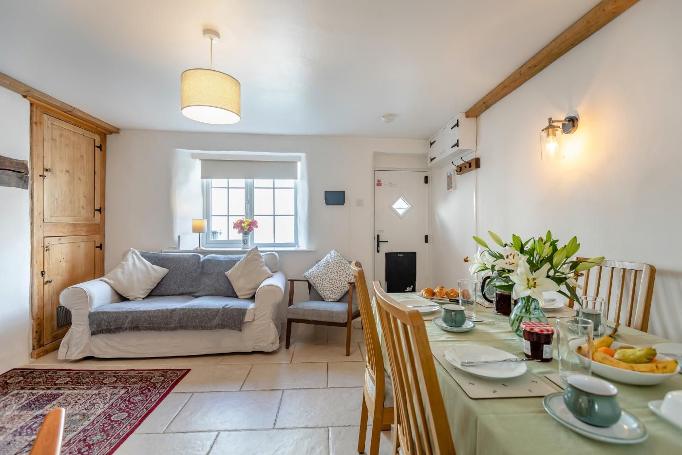 A cozy living room with a sofa, a dining table set with plates, glasses, and a vase of flowers.