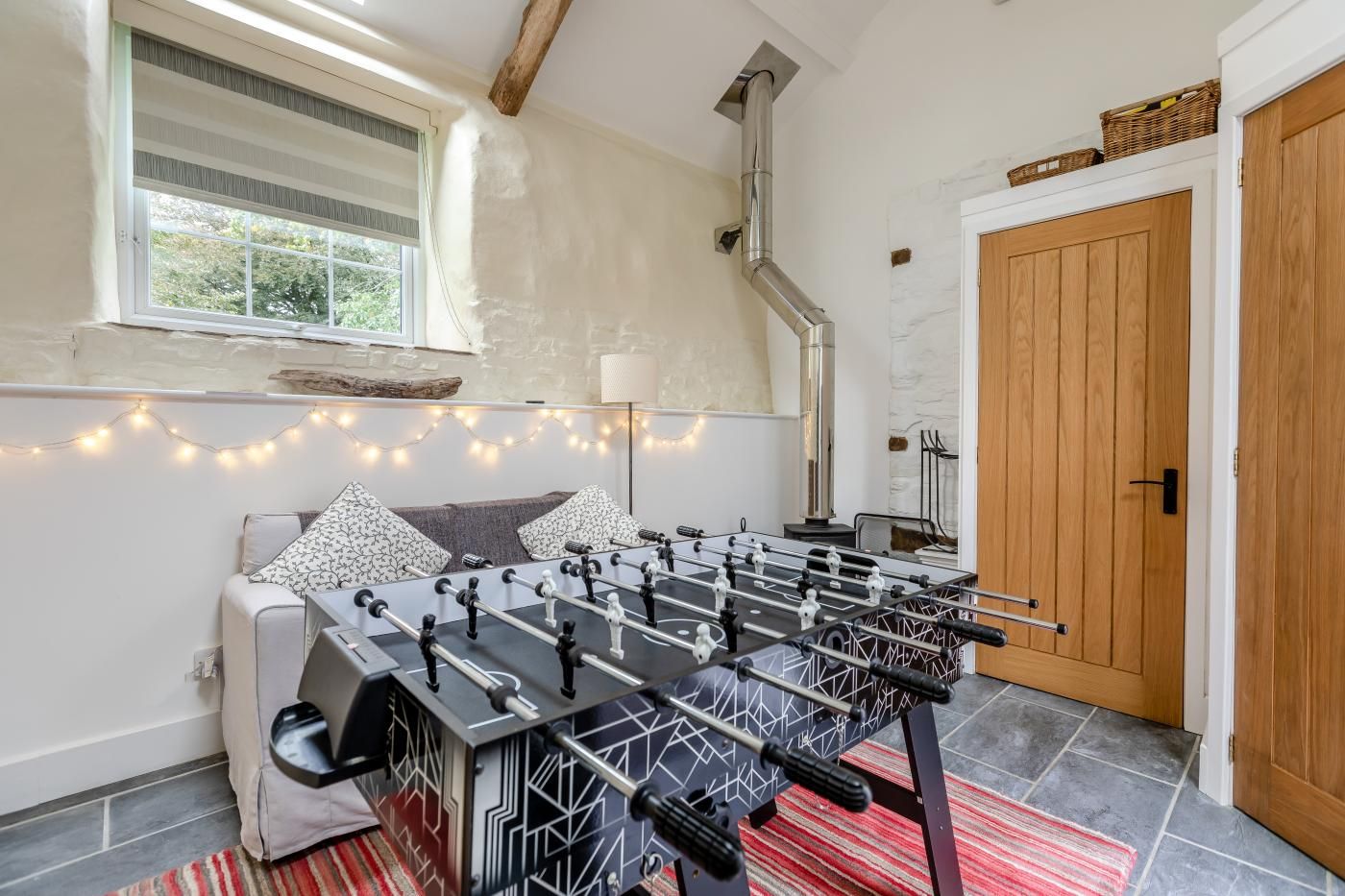 A cozy room with a foosball table, a window with curtains, a wooden door, and a fireplace.
