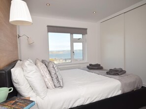 A bedroom with a bed, pillows, a bedside table with a book, a lamp, and a window with a view. - 4 Bed in Bideford (oc-55573) (Appledore)