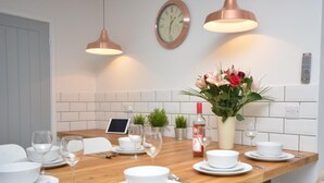 Ein Essbereich mit einem Holztisch, gedeckt für eine Mahlzeit, einer Wanduhr und einem Blumentopf mit Blumen.