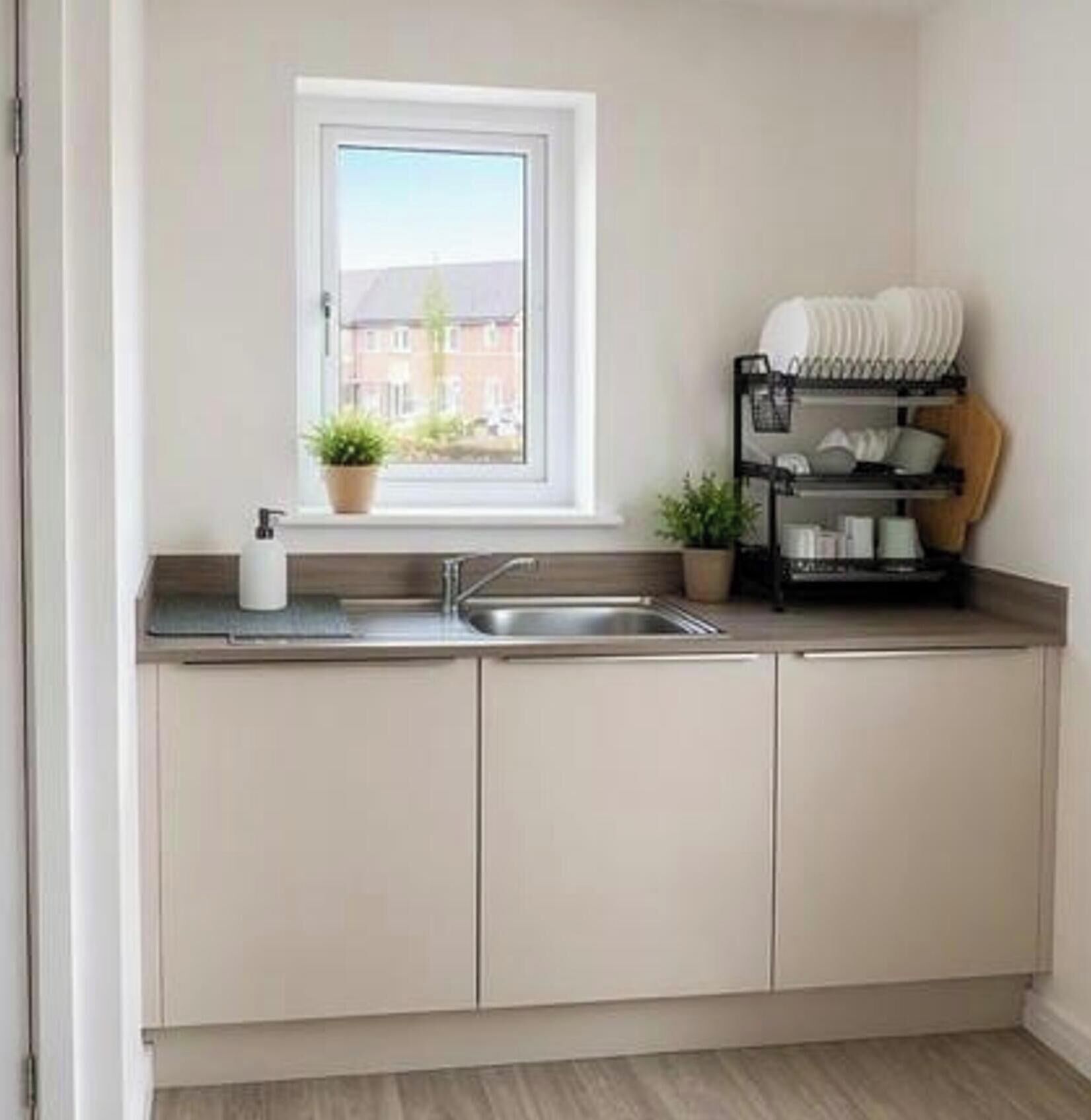 A modern kitchen with a window, a sink, cabinets, and a dish rack.