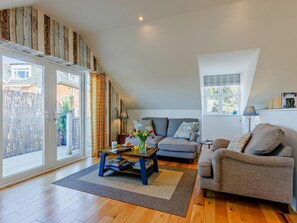 Ein geräumiges Wohnzimmer mit einer Couch, einem Couchtisch und einem Esstisch. Eine Glastür öffnet sich zu einem Außenbereich.