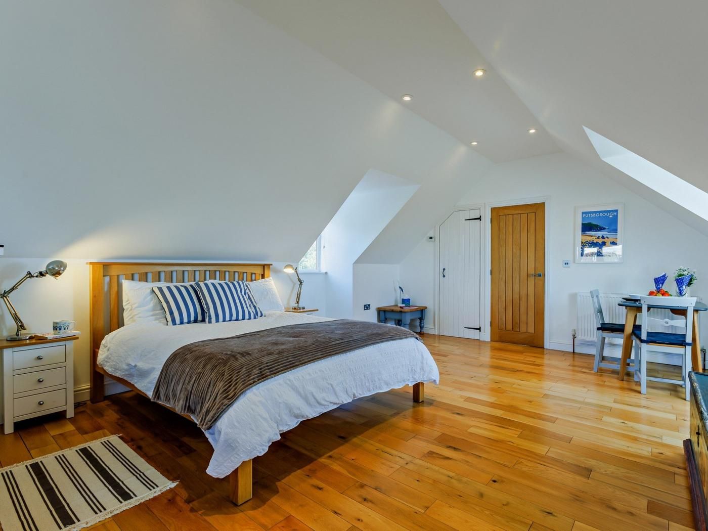 A bedroom with a sloped ceiling, a bed with a wooden headboard, a nightstand, a desk, a chair, and a radiator.