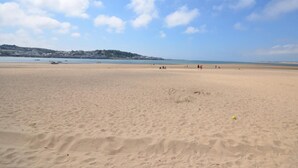 Une vaste plage de sable, avec un ciel dégagé et des bâtiments qui se dessinent à l’horizon.
