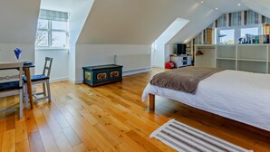 Une chambre avec un plafond en pente, un lit, un bureau avec une chaise, un radiateur et une fenêtre.