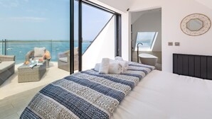 Ein Schlafzimmer mit großem Bett, Meerblick, einem Balkon mit Korbmöbeln und einem modernen Badezimmer.