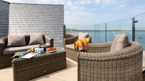 Ein Balkon mit Korbmöbeln, einem Glastisch und Blick aufs Meer.