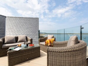 Ein Balkon mit Korbmöbeln, einem Glastisch und Blick aufs Meer.