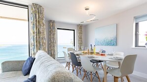 Ein moderner Essbereich mit Meerblick, eine Couch mit Kissen und ein Tisch, gedeckt für eine Mahlzeit.