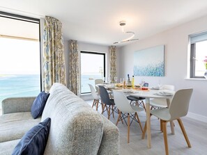 Ein moderner Essbereich mit Meerblick, eine Couch mit Kissen und ein Tisch, gedeckt für eine Mahlzeit.