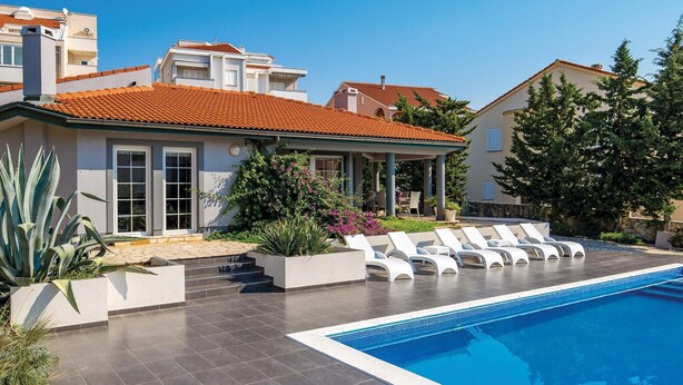 Una casa moderna amb piscina, zona de seients a l'exterior i jardí ben cuidat.