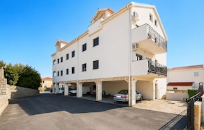 A multi-story building with a parking area in front, featuring a flat roof and a balcony on the upper floor. - Nice apartment in Povljana with WiFi (Povljana)