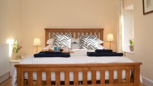 A bed with a wooden frame, two pillows with a black and white pattern, bedside lamps, a window with a view, and a small potted plant on the windowsill. - 2 Bed in Ilminster (oc-56523) (Dowlish Ford)