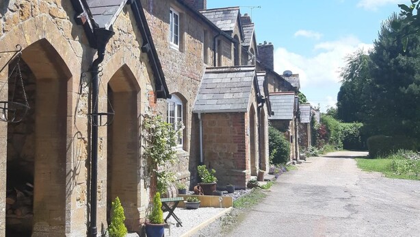 A row of stone buildings with arched doorways, a gravel path, and potted plants. - 2 Bed in Ilminster (oc-56523) (Dowlish Ford)