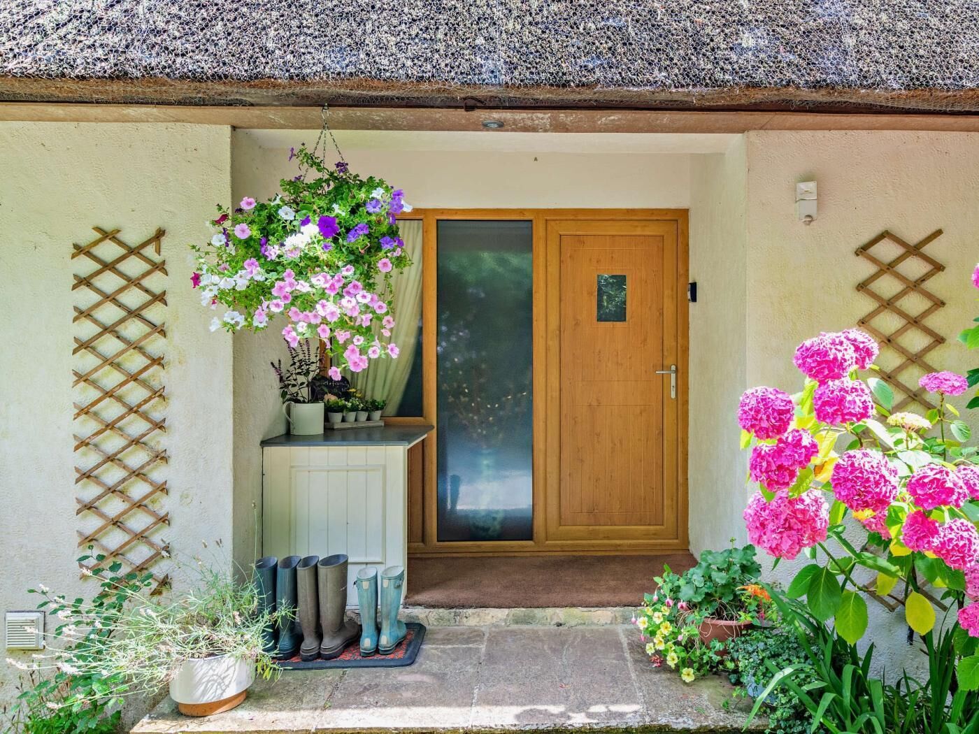 A wooden door with a glass panel, a white wall with a lattice design, and a hanging flower basket.