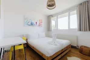 Een hotelkamer met een bed, een bureau, een stoel, een raam met gordijnen en een stadsgezichtschilderij aan de muur.