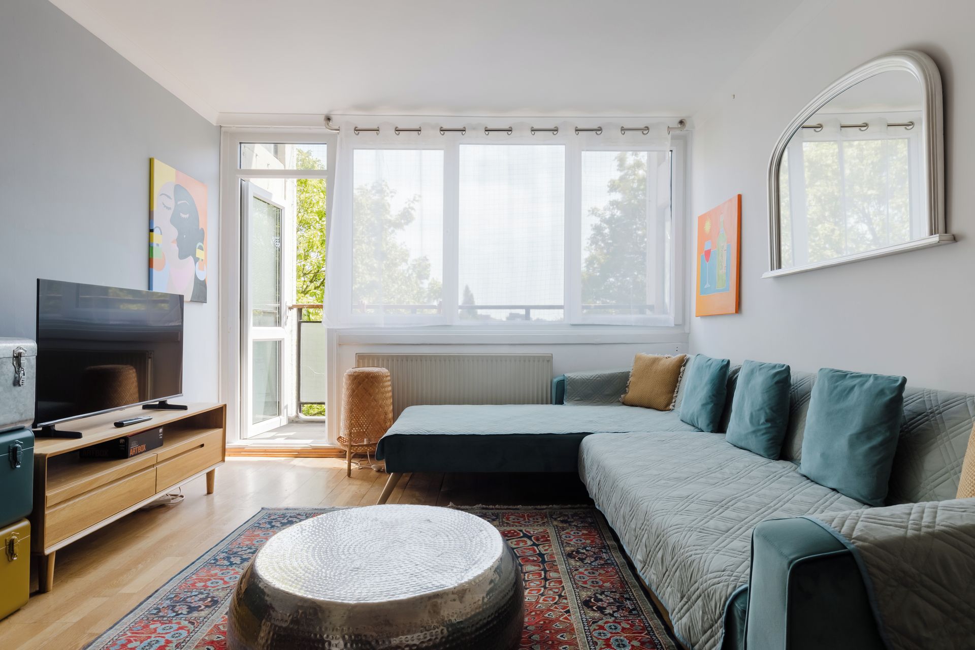 Una sala de estar moderna con un sofá modular, un televisor, una mesa de centro redonda y un ventanal con cortinas.