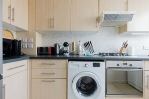 Een functionele keuken met een wasmachine, kookplaat en magnetron.