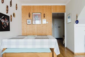 Une chambre avec un lambris en bois, un lit recouvert d’une courtepointe à carreaux et divers éléments de décoration murale, notamment des masques et des tableaux encadrés.