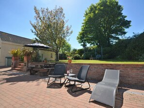 An outdoor patio with a table and chairs, a grill, and a tree. - 5 Bed in Tenby (oc-56683) (Penally)