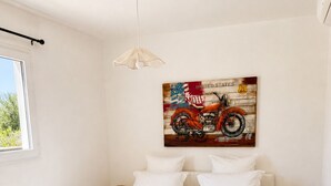 Ein Schlafzimmer mit einem Bett, Kissen, einem an der Wand befestigten Motorradbild, einem Fenster und einer Pendelleuchte.