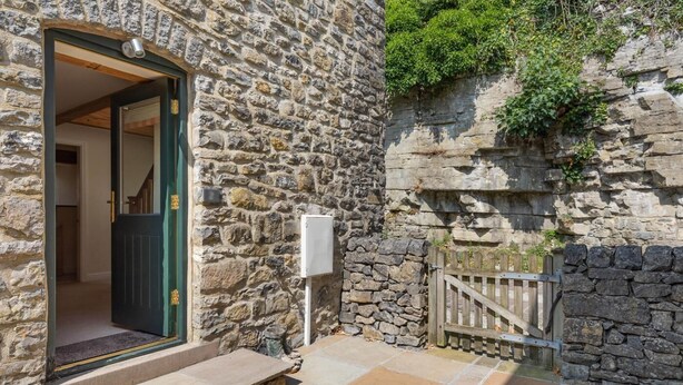 A stone building with a wooden gate, a door, and a stone wall with greenery. - 3 Bed in Buxton (oc-57037) (Cressbrook)