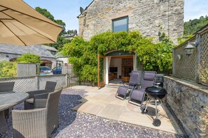 Ein Steinhaus mit einer Terrassenfläche, ausgestattet mit Korbmöbeln, einem Grill und einer Sat-Anlage.