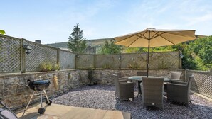 An outdoor patio area with a stone wall, a barbecue grill, wicker furniture, and a large umbrella. - 3 Bed in Buxton (oc-57037) (Cressbrook)