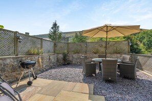 Eine Außenpatio-Terrasse mit einer Steinwand, einem Grill, Korbmöbeln und einem großen Sonnenschirm.