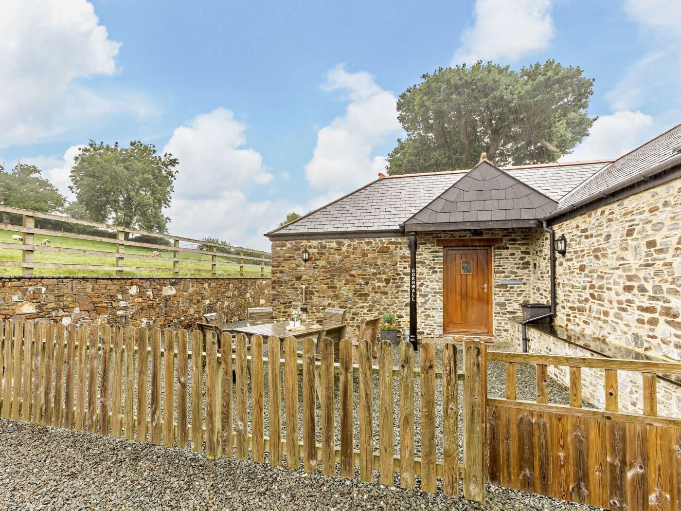 A stone building with a wooden door, a gravel path, and a wooden fence.