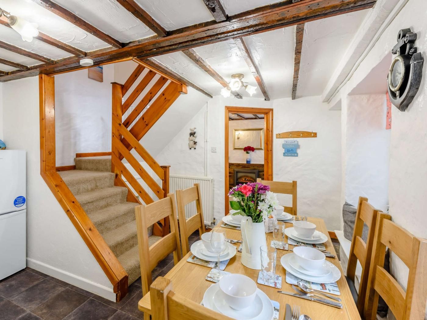A dining area with a wooden staircase, a table set for four, and a mirror on the wall.