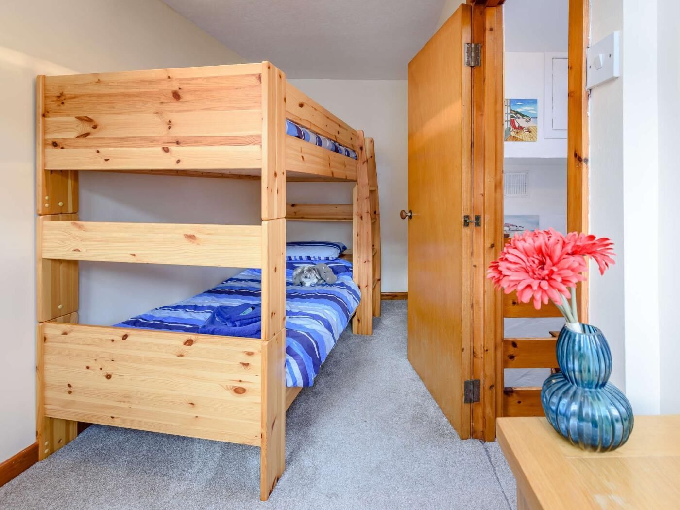 A bunk bed room with a wooden door, a small table with a vase, and a carpeted floor.