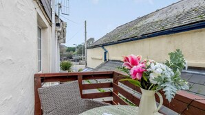 A balcony with wicker furniture, a table with a book, and a vase with flowers. - 3 Bed in Ilfracombe (oc-57795) (Ilfracombe)